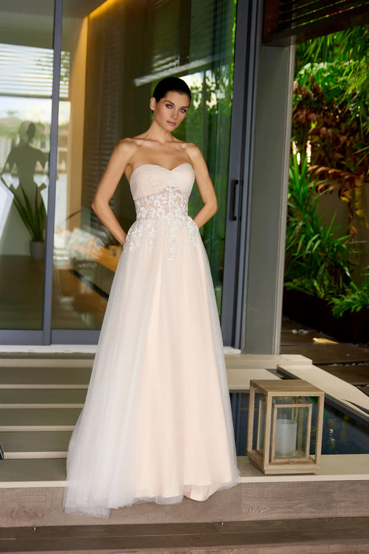 Woman in a nude strapless wedding gown standing on a staircase with greenery in the background