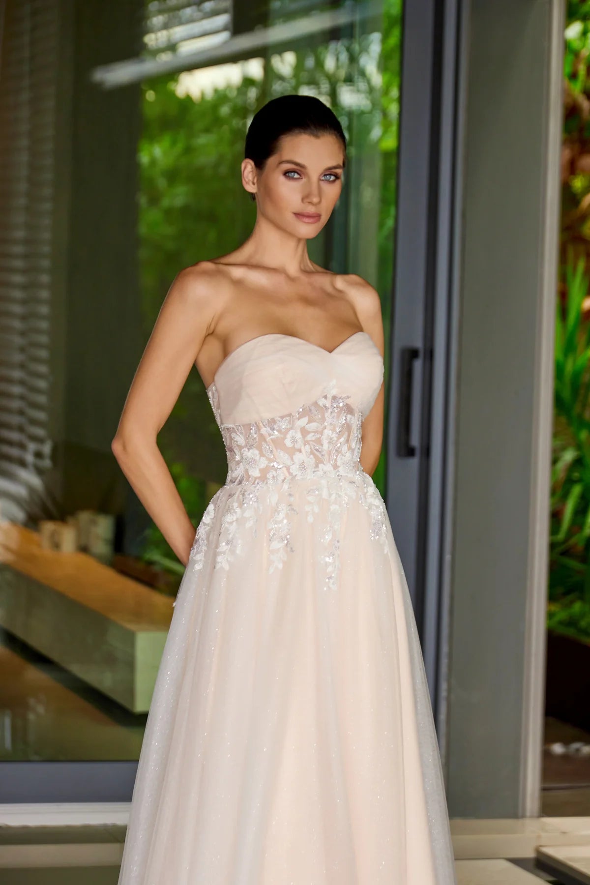 Woman wearing a strapless nude wedding gown with floral details in an outdoor setting.