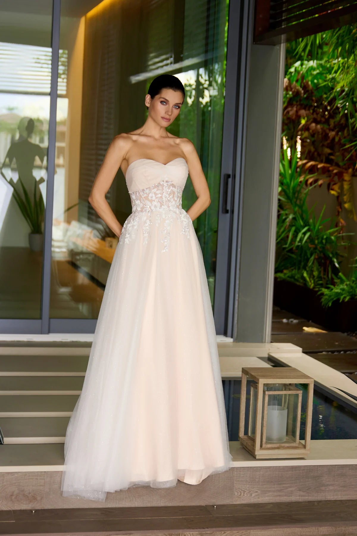 Woman in a nude strapless wedding gown standing on a staircase with greenery in the background