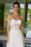 Woman wearing a strapless white wedding dress with lace detailing in an outdoor setting.
