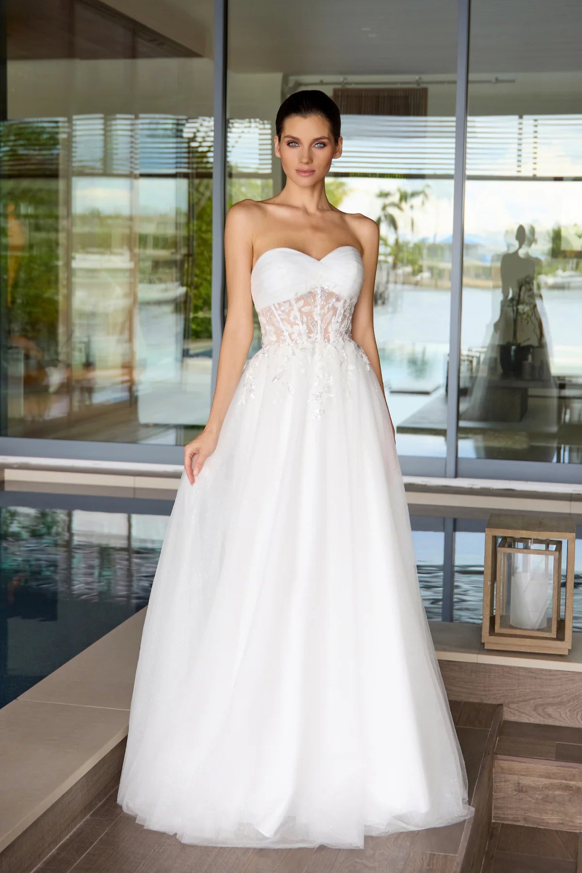 Woman in a white wedding dress standing in a modern indoor setting with large windows.