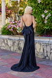 A woman with long blonde hair stands outdoors by flowers, wearing the Juliet JT2728H Long Prom Dress—featuring a tight fit, open back, large bow, and floor-length train.