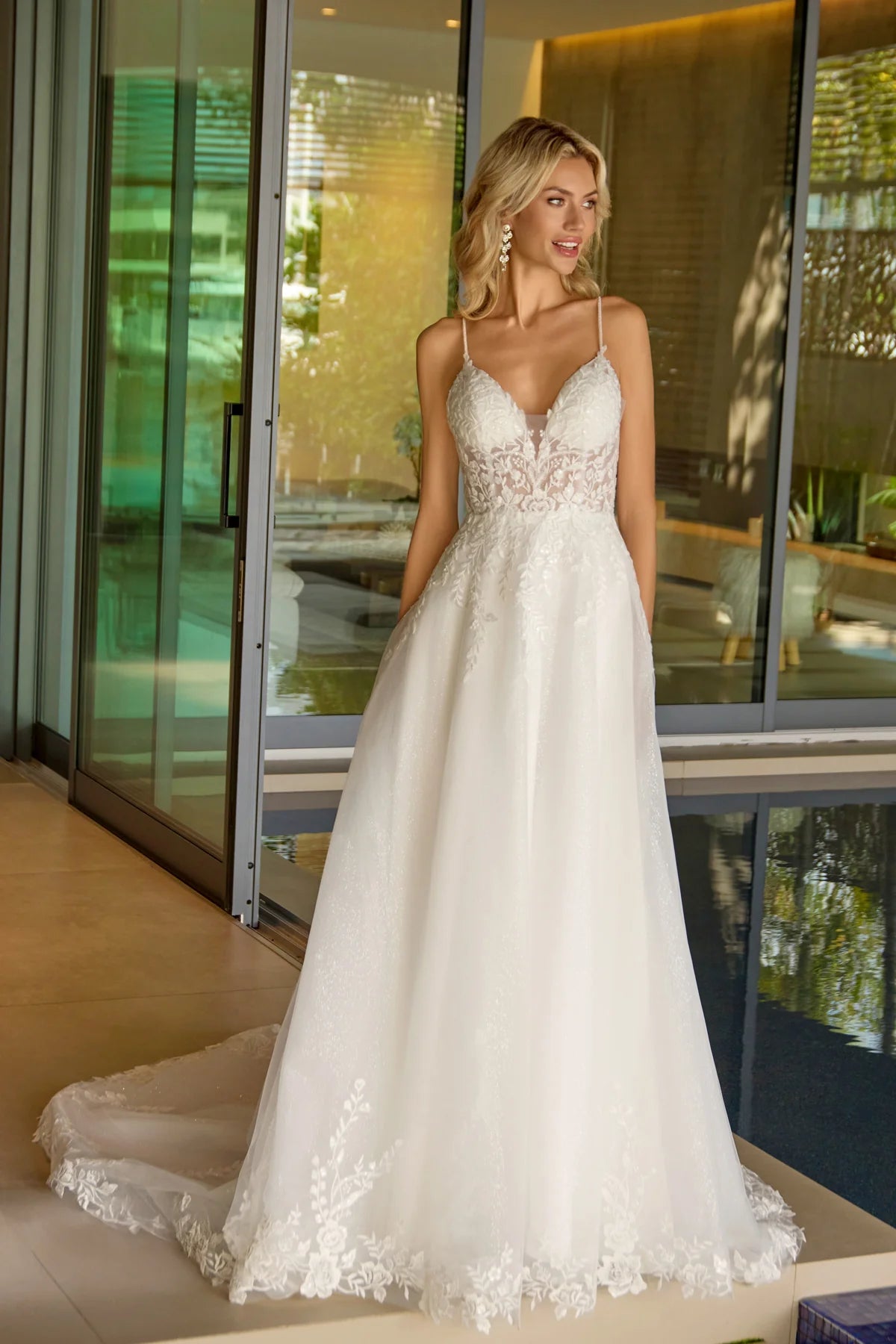 Woman in a white wedding dress standing indoors with large windows in the background