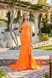 A woman stands outdoors in front of a stone walkway and vine-covered pergola, wearing the Juliet JT2727H Long Prom Dress—a fitted, bright orange gown with ruffle details and a flattering corset bodice.