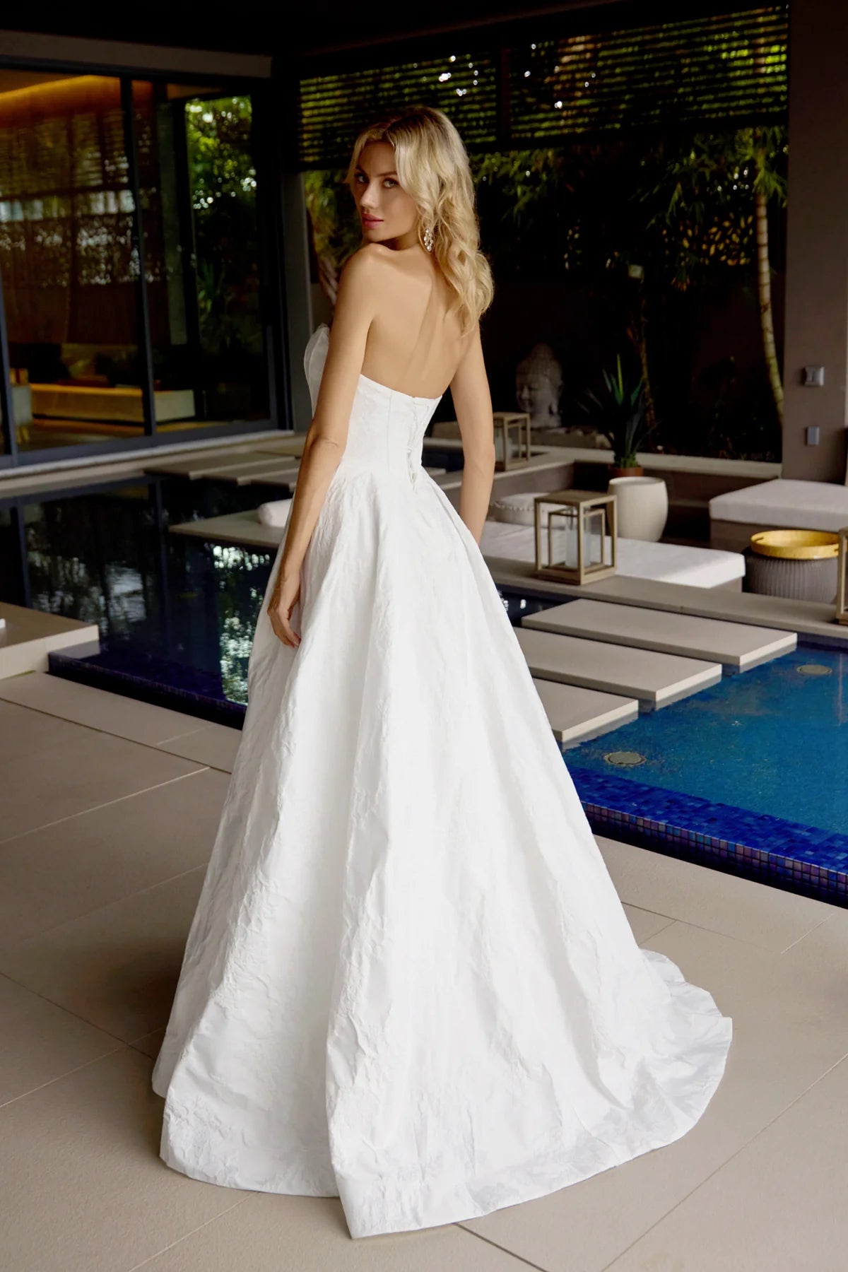 Woman in a white dress standing by a poolside.