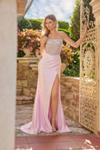 Wearing the Long Prom Dress: Juliet JT2729H, a woman in a strapless corset gown with a beaded bodice and high leg slit stands outdoors beside a decorative gate and blooming flowers.