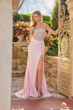 Wearing the Long Prom Dress: Juliet JT2729H, a woman in a strapless corset gown with a beaded bodice and high leg slit stands outdoors beside a decorative gate and blooming flowers.