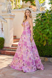 A woman in a Pink Floral Juliet JT2735H Long Prom Dress stands outside by steps, with greenery and decorative statues in the background.