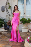 A woman in the Juliet JT2698A long fuchsia prom dress, featuring a strapless satin corset bodice and high slit, stands on a stone patio before a window and potted plants.