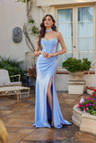 A woman stands outdoors in the Perry Blue Juliet JT2698A long prom dress, featuring a strapless satin corset bodice and thigh-high slit, styled with a choker necklace and high heels amid lush plants and patio decor.
