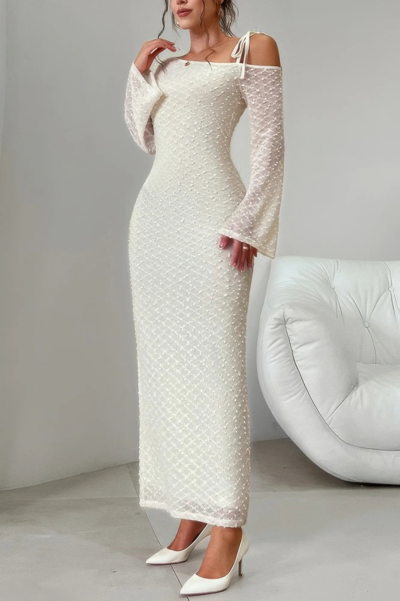 Woman wearing a white lace dress with long sleeves in a minimalistic setting.