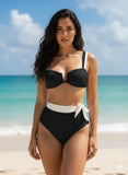 Woman in a black bikini with white accents standing on a beach.