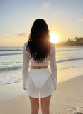Woman in a white outfit standing on a beach at sunset