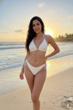 Woman in a white bikini standing on a beach with sunset in the background