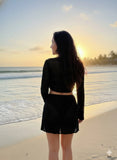 Woman in a black outfit standing on a beach at sunset