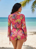 Woman in a colorful floral swimsuit on a beach with palm trees and blue sky.